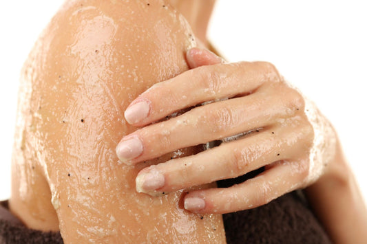 A woman demonstrates how to use a body scrub, holding her arm covered with a towel.